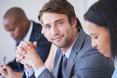 Buy stock photo Portrait of a young businessman sitting in a meeting with his colleagues