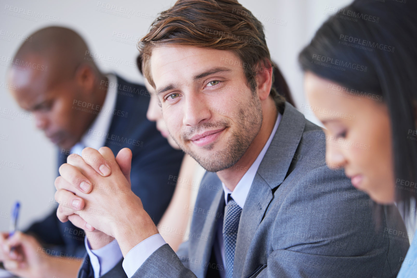 Buy stock photo Portrait of a young businessman sitting in a meeting with his colleagues