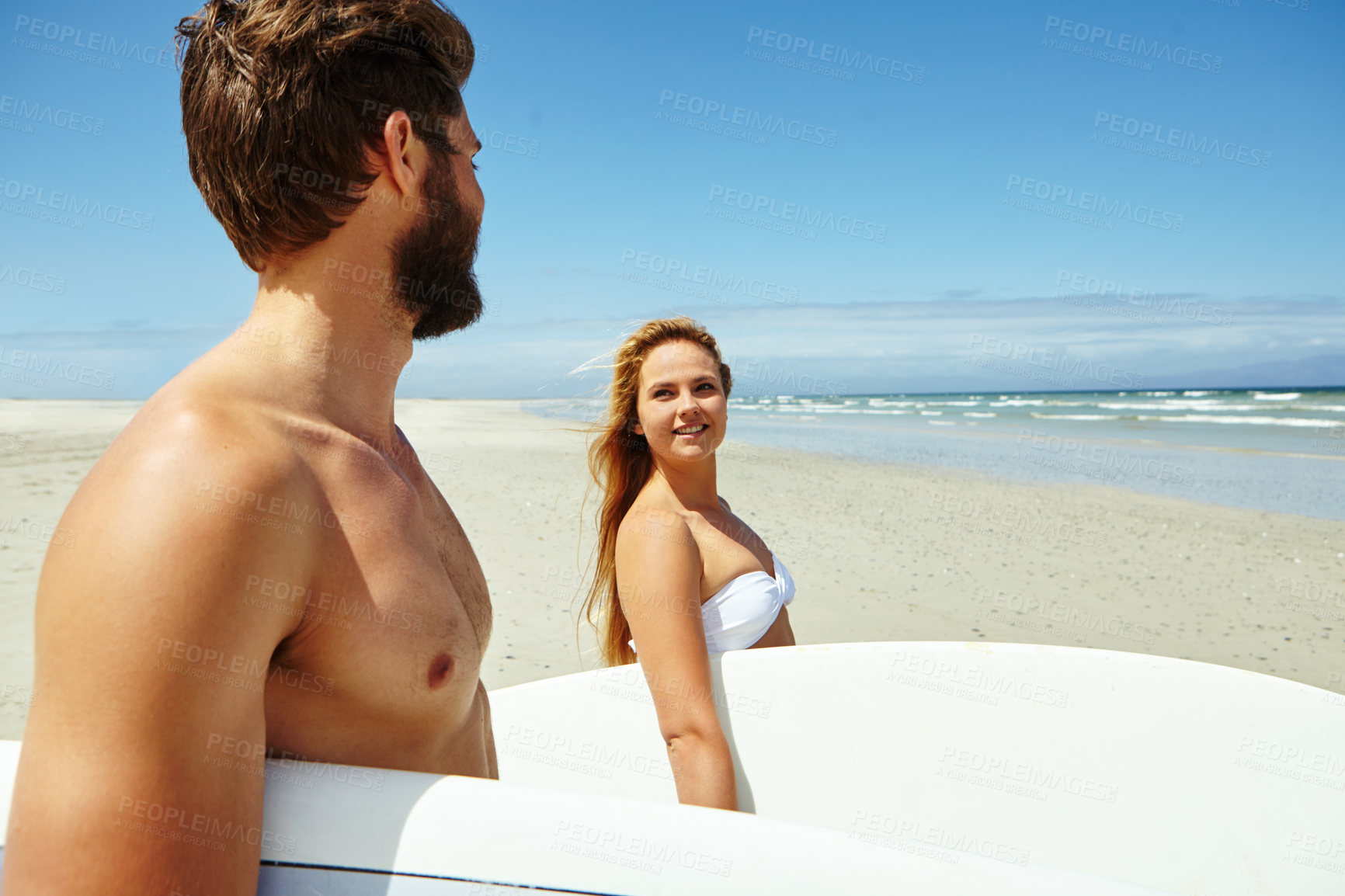 Buy stock photo Shot of a young couple walking on the beach, carrying their surfboards