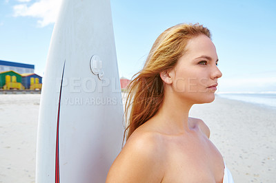 Buy stock photo Shot of a young woman standing on the beach with her surfboard looking out at the ocean