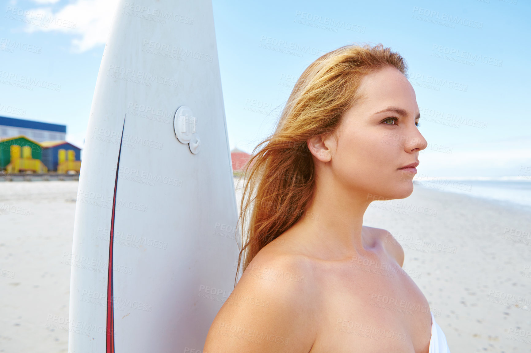 Buy stock photo Shot of a young woman standing on the beach with her surfboard looking out at the ocean