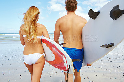 Buy stock photo Rearview shot of a young couple heading out into the ocean with their surfboards