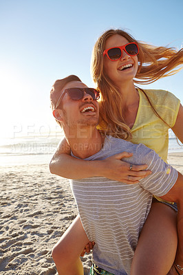 Buy stock photo Shot of a handsome young man giving his girlfriend a piggyback at the beach