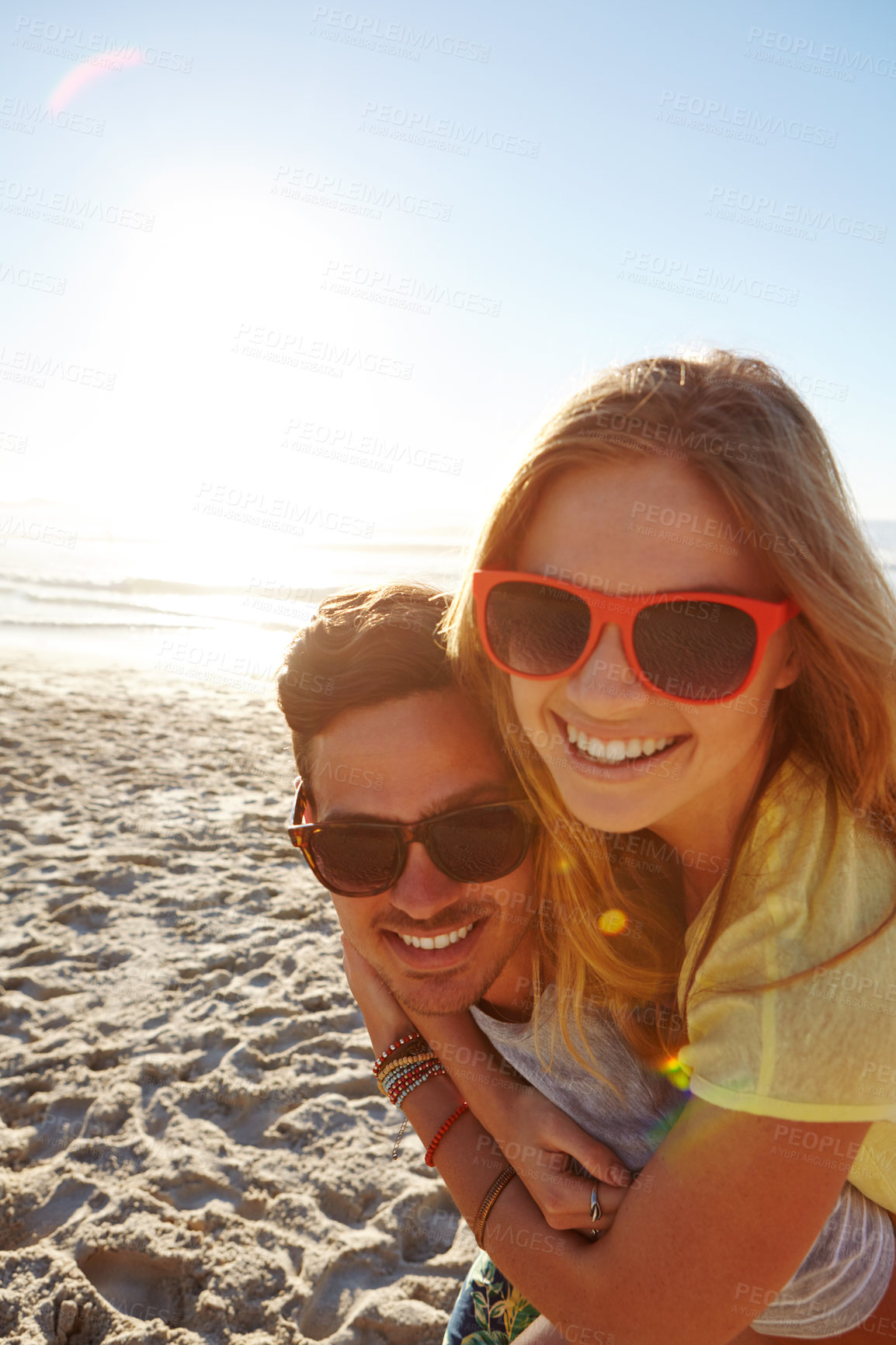 Buy stock photo Portrait of a handsome young man giving his girlfriend a piggyback at the beach