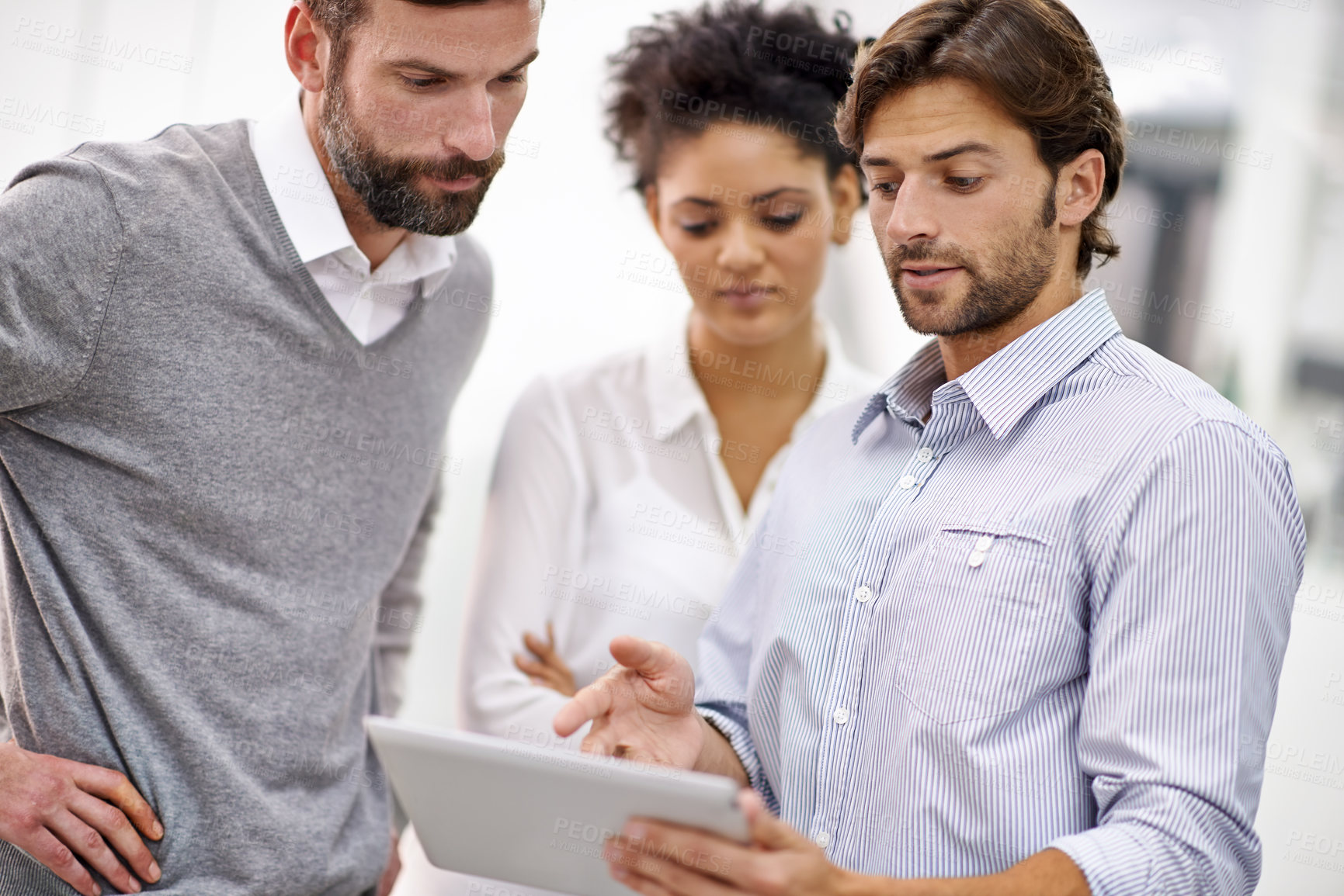 Buy stock photo Shot of three young businesspeople standing in his office and talking over a tablet