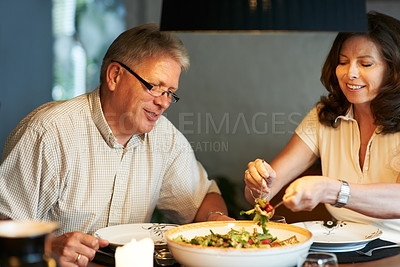 Buy stock photo Mature couple, eating together at table with food and love in marriage with happiness in home. Lunch, old man and woman with smile, diet and salad for dinner in house with kindness, bonding and meal.