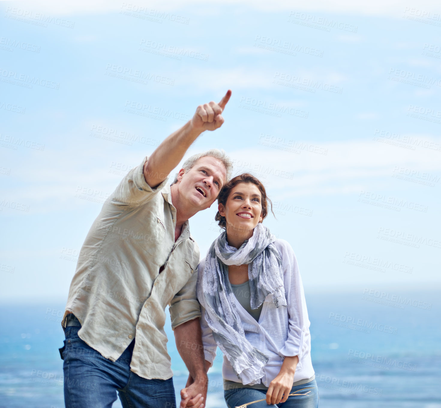 Buy stock photo Pointing, happy couple and travel together at the beach with love, adventure and summer. Vacation, man and woman holding hands and sightseeing at ocean, offshore or enjoy holiday with support or care