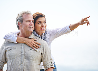 Buy stock photo Happy, mature couple and pointing on holiday with travel to beach and embrace with love on adventure in summer. Vacation, sightseeing and woman hug man in nature on blue sky with mock up space