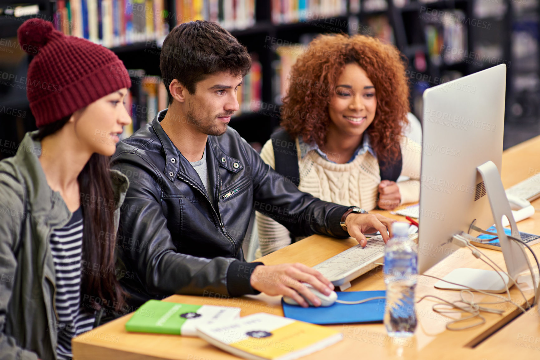 Buy stock photo Shot of a group of students working together at a computer in a university library