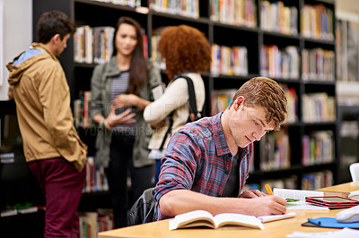 Buy stock photo Shot of a male student studying in a university library with his peers in the background