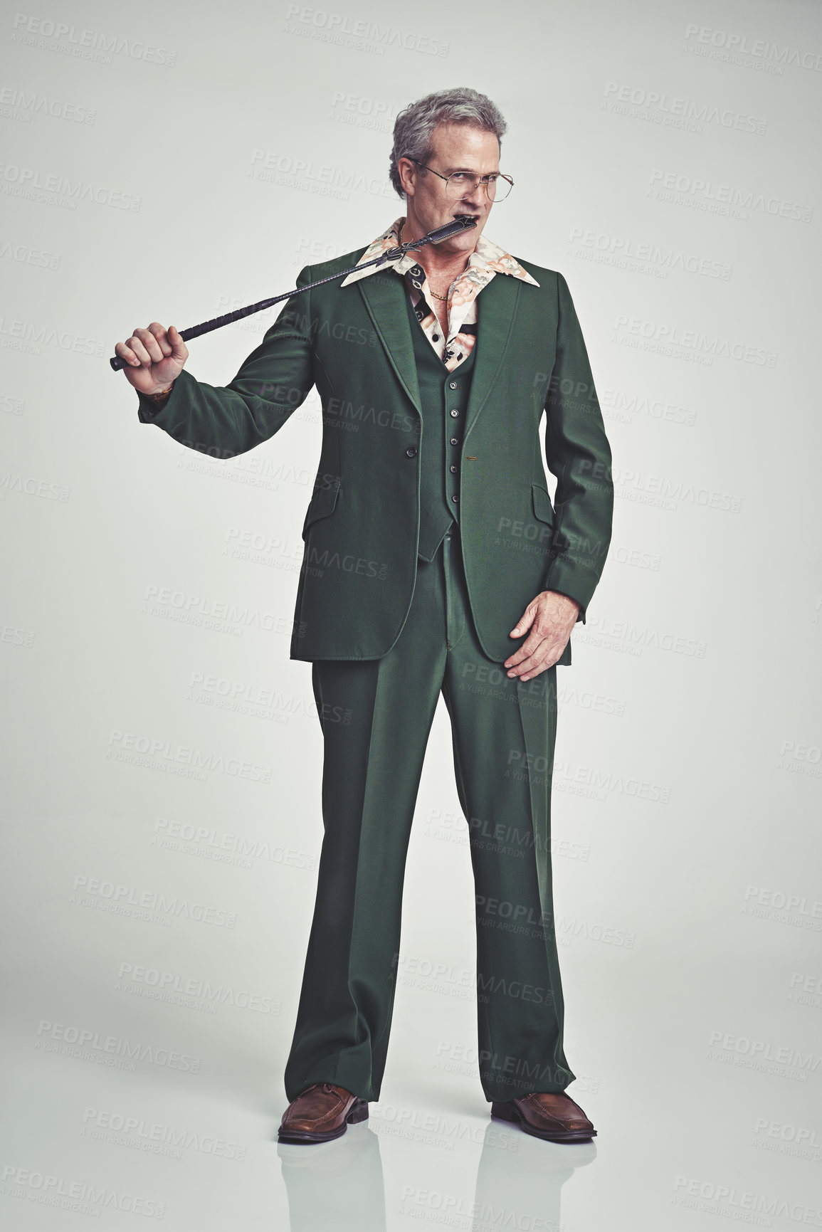 Buy stock photo Studio shot of a mature man in a retro suit biting the tip of a riding crop