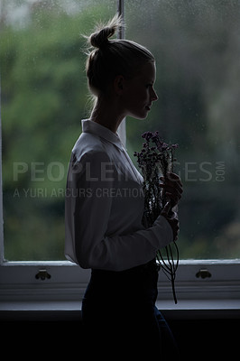 Buy stock photo Woman, flowers and window for in home, dark room and mysterious aesthetic for person or artistic pose. Female artist, dim light and silhouette with thinking, fashion and morning setting in dawn