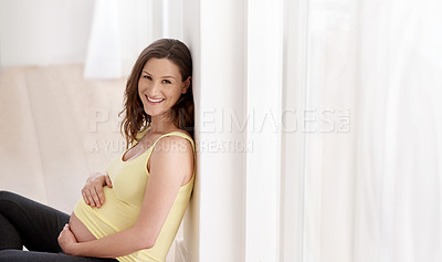 Buy stock photo Shot of a young pregnant woman sitting on her living room floor