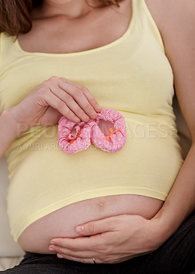 Buy stock photo Shot of a young pregnant woman holding a pair of pink baby shoes against her belly