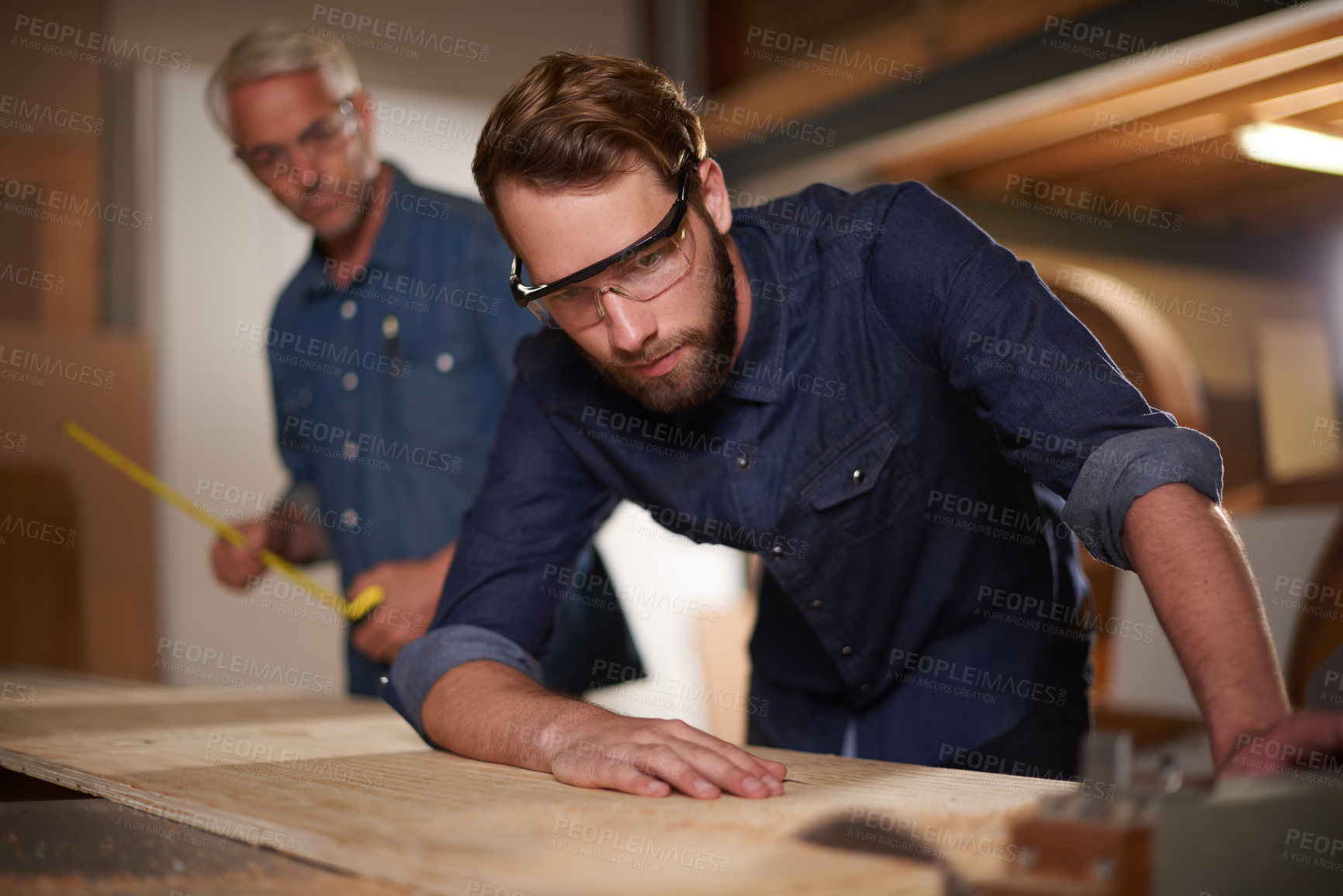 Buy stock photo Carpenter, team and man with wood saw for planning construction project or senior father teaching son. Machine apprentice and mentor in woodwork, training and learning at workshop with plank on table