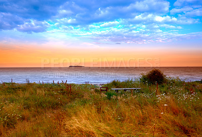 Buy stock photo Landscape, field and sunrise on beach in nature with clouds for agriculture, morning horizon and plants in countryside. Ocean, bench and sunset with scenery, ecology and growth for travel location