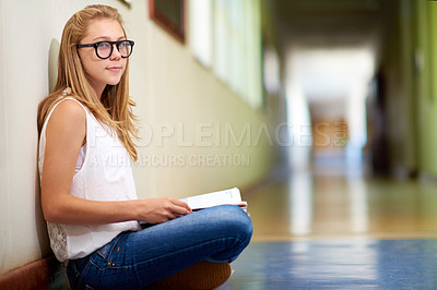 Buy stock photo Happy woman, teenager and student with book in hallway at school for learning, education or studying. Portrait of female person or young child sitting on floor in corridor with textbook by classroom