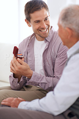 Buy stock photo Senior dad, son and medal for surprise present, support and congratulations with celebration and bonding at home. Men in living room, family with reward or award as gift for happiness and gratitude