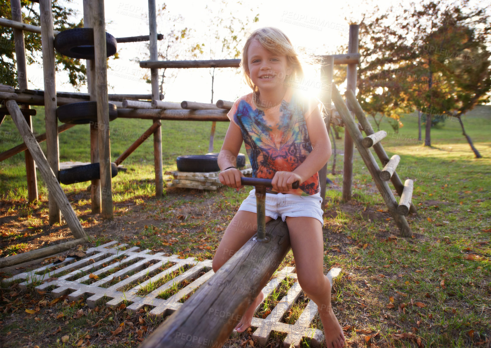 Buy stock photo Happy girl, portrait and riding seesaw in park sunset for fun holiday, weekend or outdoor break in nature. Face of female person, kid or child smile on playground for childhood activity outside