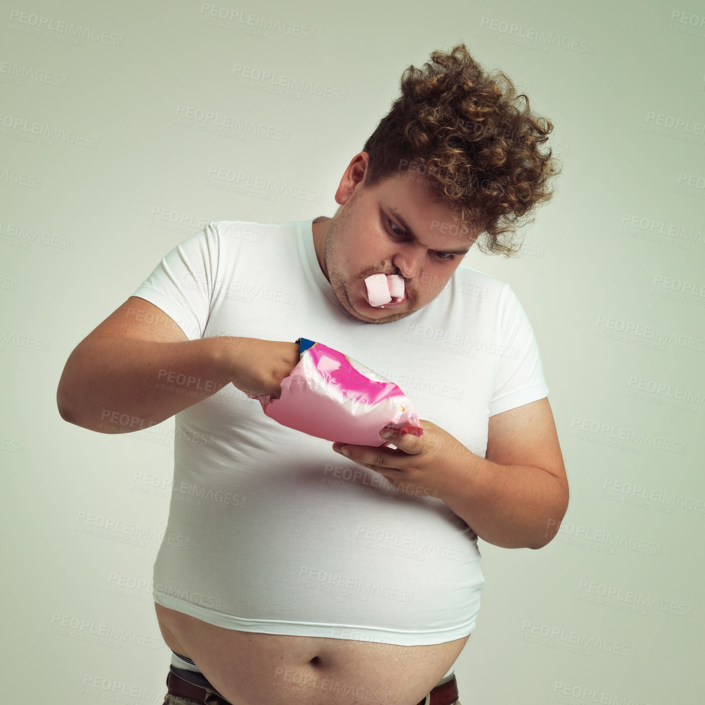 Buy stock photo Food, hunger and marshmallow with plus size man in studio on gray background for unhealthy eating. Belly, hungry for sweets and candy with young person with snack bag or packet for greed or gluttony