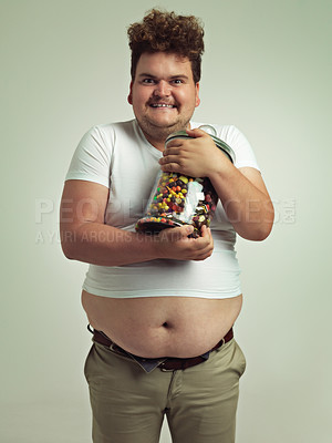 Buy stock photo Candy, crazy and portrait of plus size man in studio for luxury snacks, sweets and dessert in container. Comic, funny facial expression and isolated person with glass for unhealthy diet on background
