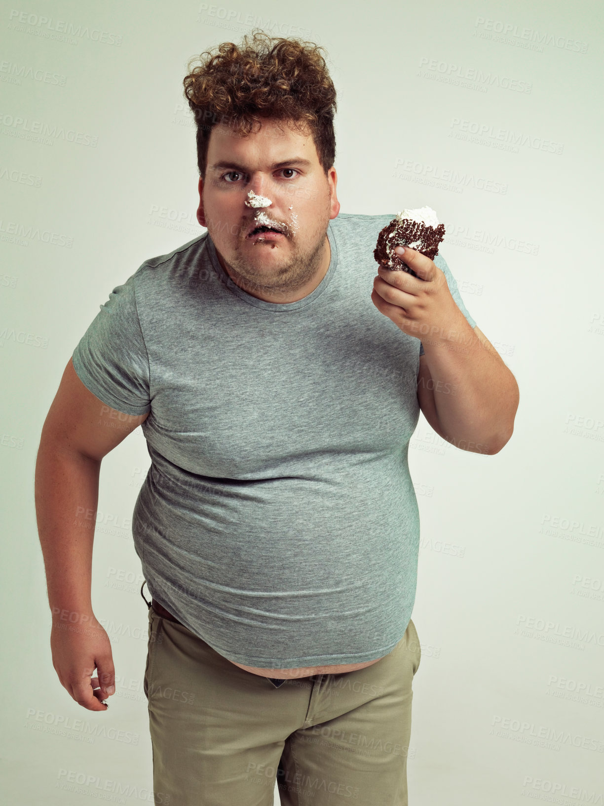 Buy stock photo Plus size, eating and portrait of man with cake in studio for unhealthy, sugar and sweet snack. Greedy, food and male person with messy slice of chocolate dessert isolated by gray background.