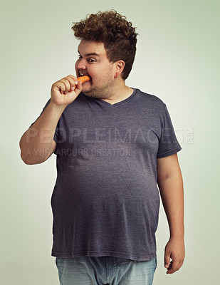 Buy stock photo Plus size, diet and man eating carrot for nutrition, health benefit and wellness in studio by white background. Weight loss, vegetable and hungry male person for detox, wellbeing and vegan food