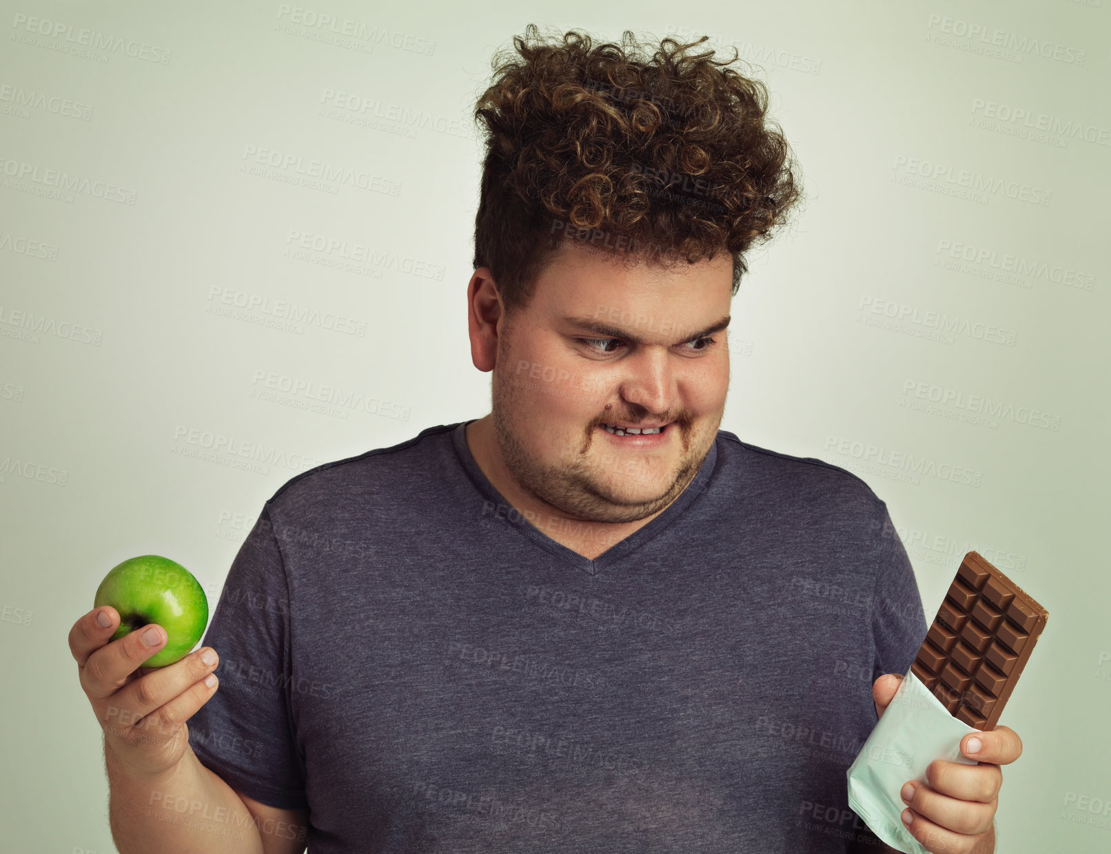 Buy stock photo Choice, man and apple with chocolate in studio with smile for diet, nutrition and food for snack. Plus size, male person and thinking with option for healthy fruit, sweet dessert and decision