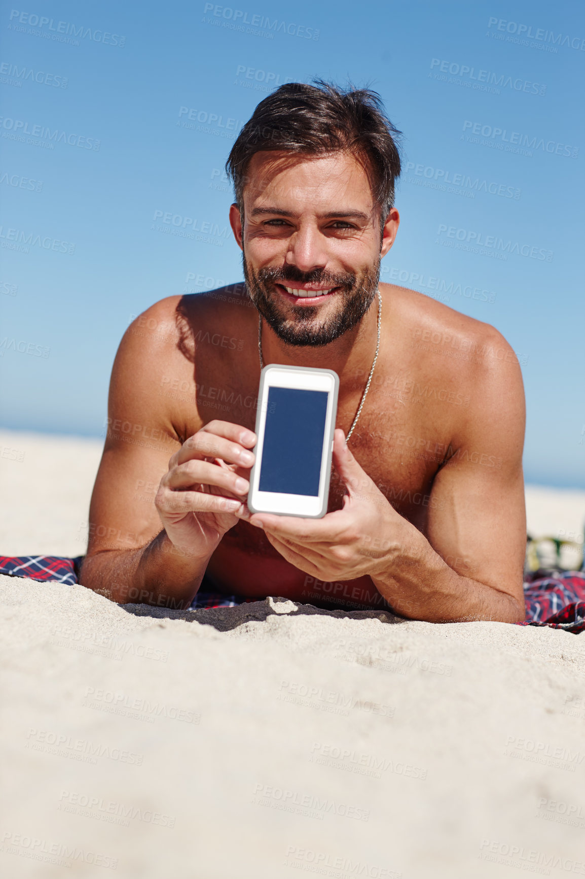 Buy stock photo Shot of a young man showing a blank cellphone screen while at the beach