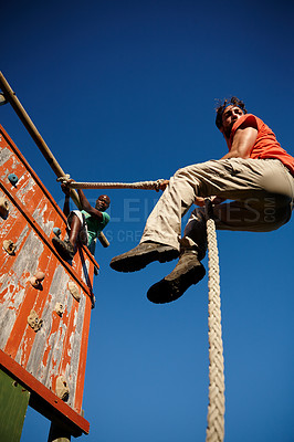 Buy stock photo Shot of a young men climbing an obstacle wall at military bootcamp