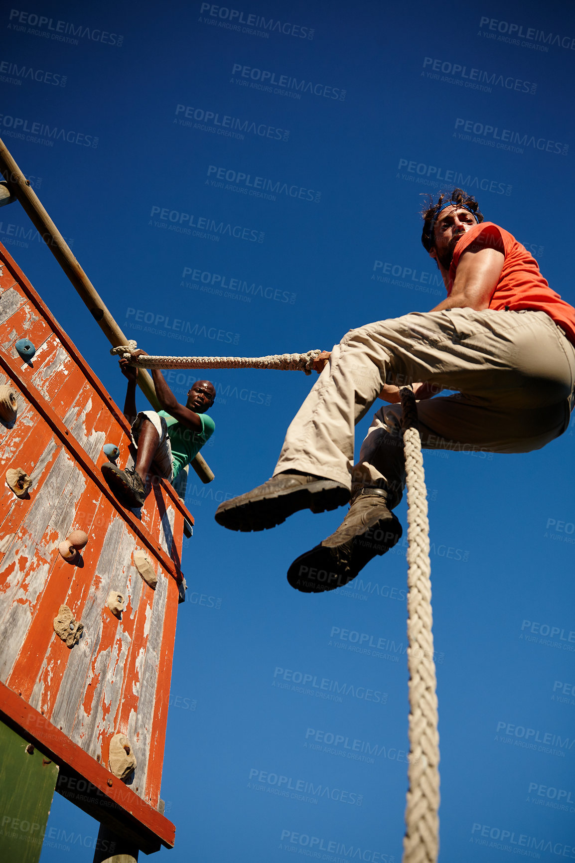 Buy stock photo Shot of a young men climbing an obstacle wall at military bootcamp