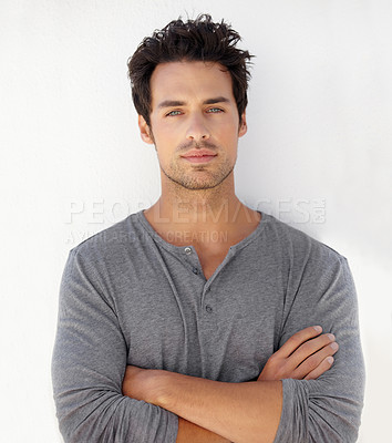 Buy stock photo Portrait of a handsome young man standing against a wall with his arms crossed