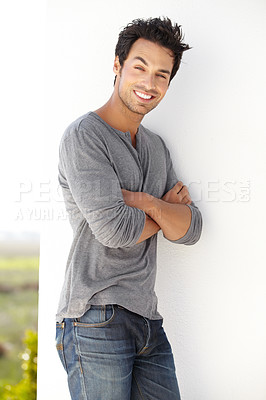 Buy stock photo Portrait of a handsome young man leaning against a wall with his arms crossed