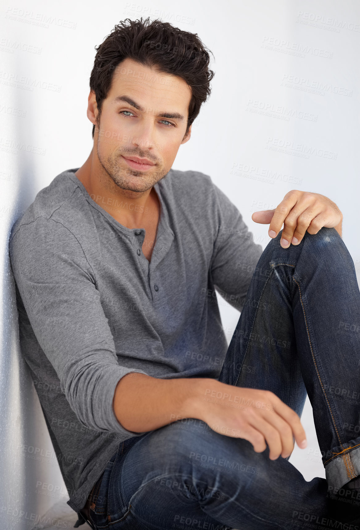 Buy stock photo Cropped shot of a handsome young man sitting on the floor leaning against a white wall