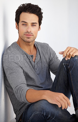 Buy stock photo Cropped shot of a handsome young man sitting on the floor leaning against a white wall