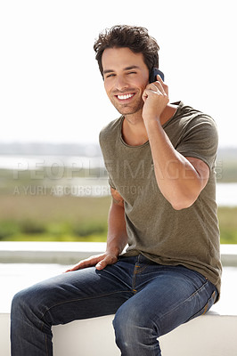 Buy stock photo Portrait of a young man talking on his cellphone while sitting on the roof of a building