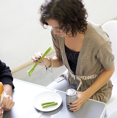 Buy stock photo Health, diet and woman eating a celery stick for weightloss, wellness or vegetarian snack. Disappointment, upset and young female person with a green vegetable and beverage by a dining table at home.