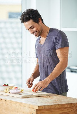 Buy stock photo Shot of a handsome young man making a fruit salad for breakfast at home