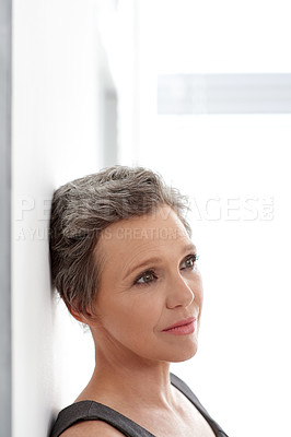 Buy stock photo A mature businesswoman looking away thoughtfully while leaning against a wall