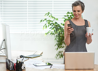 Buy stock photo A mature businesswoman checking her cellphone while having coffee at the office