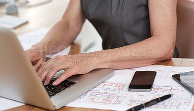 Buy stock photo Cropped image of an architect working on her laptop with building plans beside her on her desk