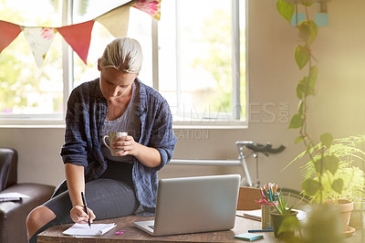 Buy stock photo A young woman writing things down on a notepad while sitting on her desk having coffee