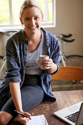 Buy stock photo A young woman writing things down on a notepad while sitting on her desk having coffee