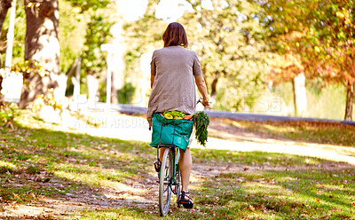 Buy stock photo Rearview shot of a young woman riding her bicycle home from the grocery store