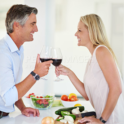 Buy stock photo Shot of an affectionate couple toasting with red wine while making dinner