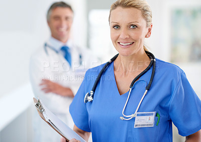 Buy stock photo Portrait of a female doctor in scrubs with a colleague standing in a the background