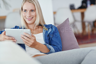 Buy stock photo Shot of an attractive young woman using a tablet while sitting on the sofa