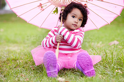 Buy stock photo Umbrella, cute and girl child in a garden sitting on the grass on summer weekend. Adorable, playful and young kid, baby or toddler with curly hair playing on the lawn in outdoor field or park.