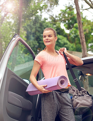 Buy stock photo Shot of a beautiful young woman carrying a yoga mat while getting out of her car