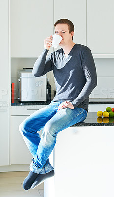 Buy stock photo Portrait of a young man sitting on his kitchen counter drinking coffee